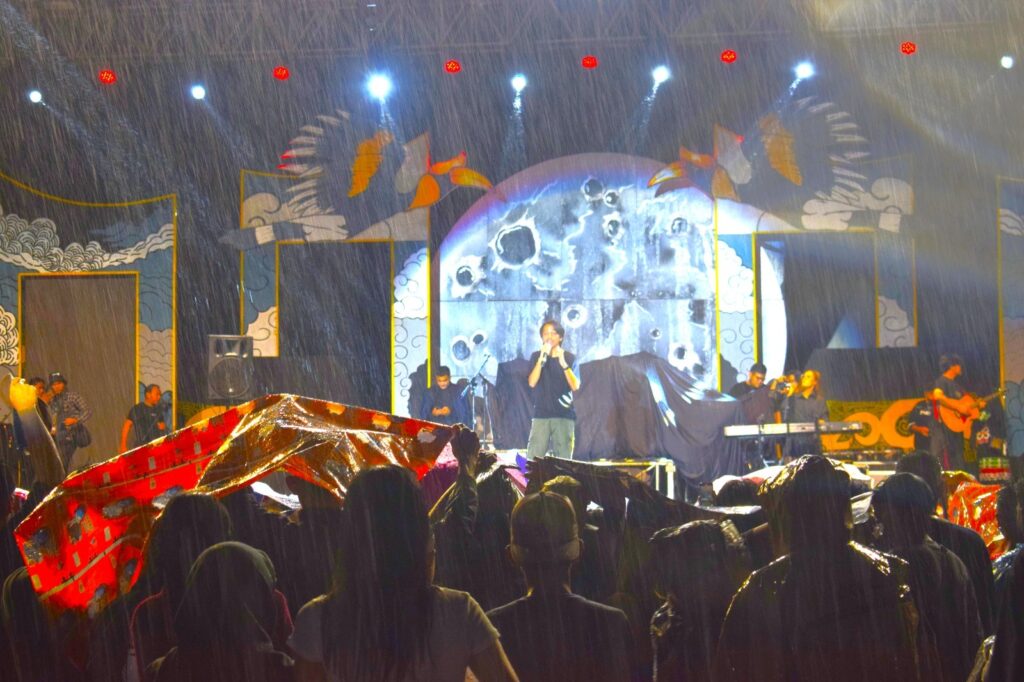 TETAP ANTUSIAS: Ribuan masyarakat tetap antusias meski sempat tertunda karena hujan deras, menyambut hangat pertunjukan musik dan tarian tradisional yang menggema di panggung utama Musik Alam Fest X Benuanta Fest 2024, Jumat (20/9/2024) malam.