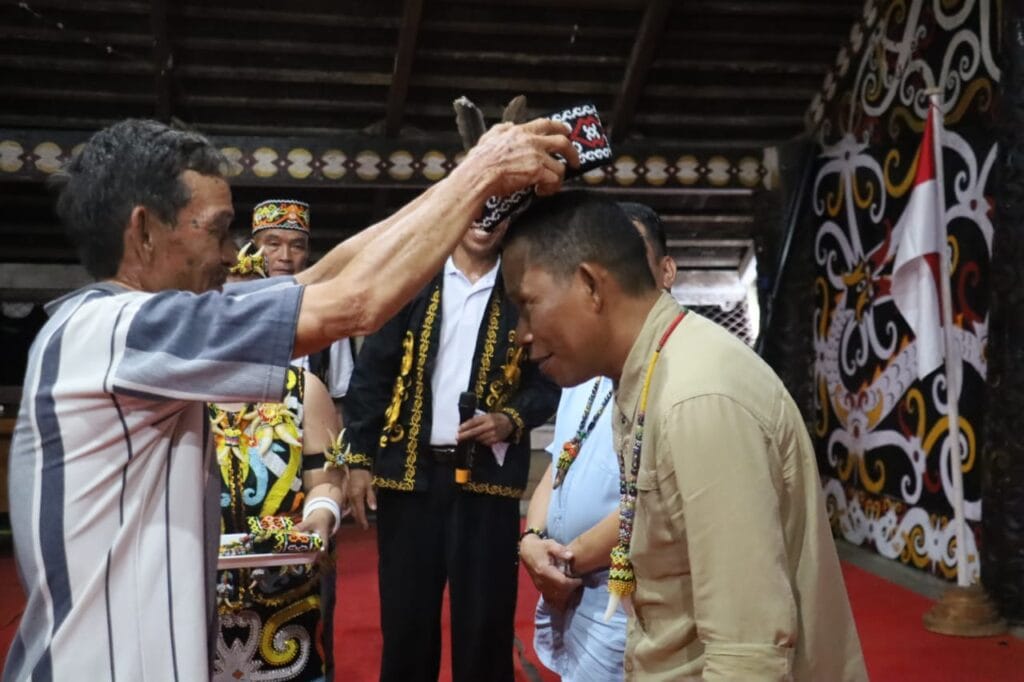 Simbol dukungan masyarakat Teras Nawang pada Paslon nomor urut 1 Syarwani-Kilat (S1AP) dengan memakaikan peci dan kalung manik pada saat kampanye, bertempat di Rumah Adat Desa Teras Nawang belum lama ini.